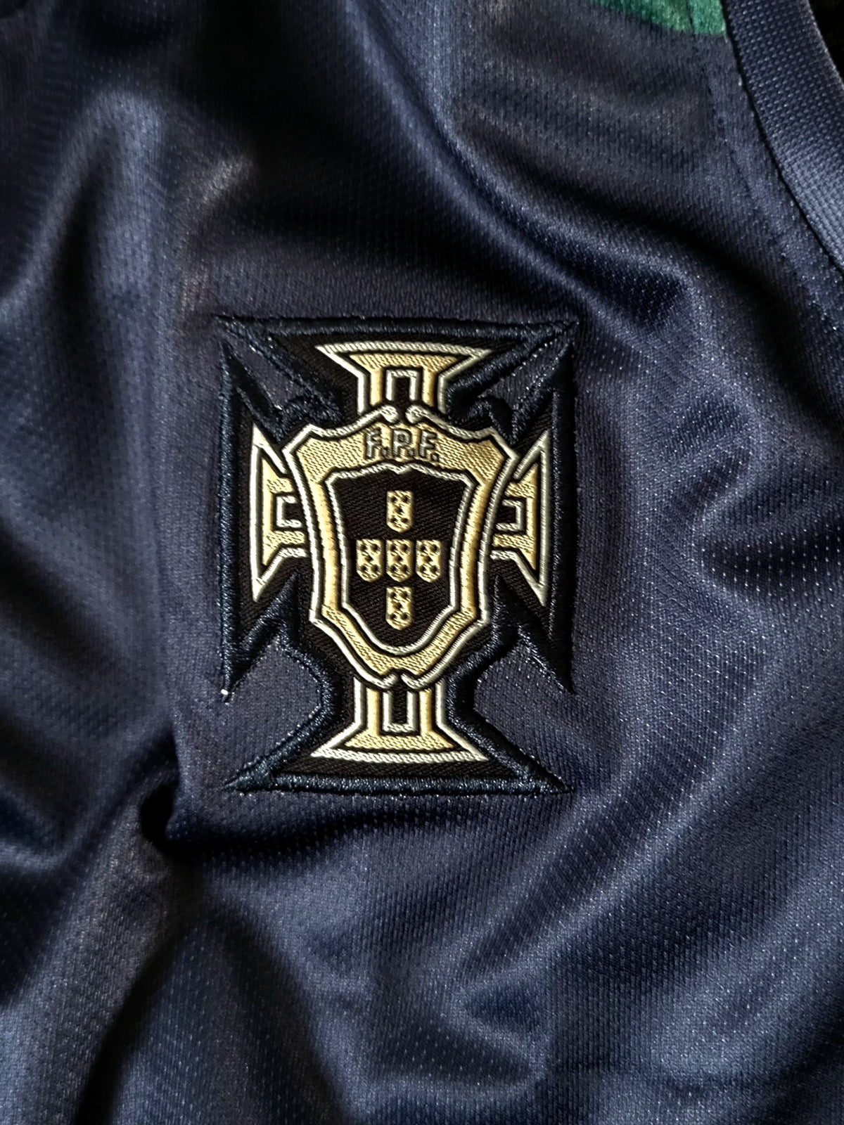 Close-up of a dark navy Portugal football jersey with the embroidered national team crest on the chest.