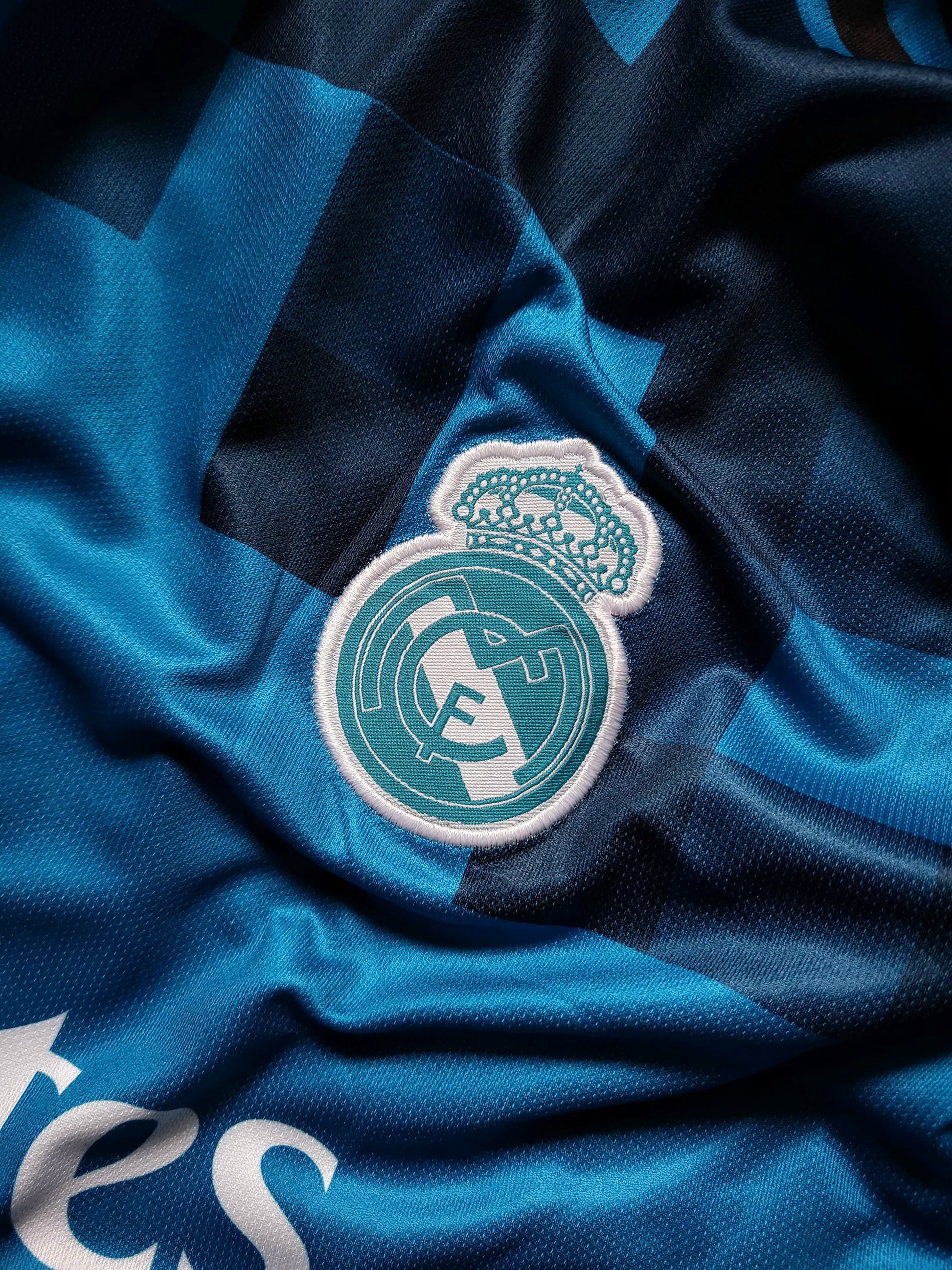 Close-up of a Real Madrid soccer jersey fabric with the club crest patch centered on a blue and navy patterned background.