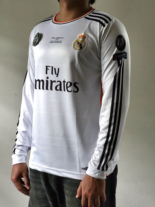 A white long-sleeve Real Madrid soccer jersey with black stripes on the sleeves and 'Fly Emirates' printed on the front, worn by a model.