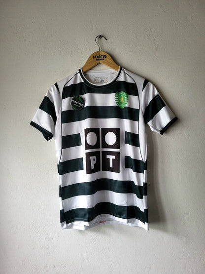 A black and white horizontally striped soccer jersey hanging on a wooden hanger against a textured gray wall. The jersey features a green and white crest on the left chest, a black circular patch on the right chest, and a large black 'PT' logo with white circles in the center.