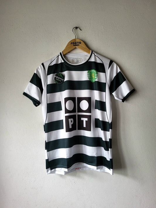 A black and white horizontally striped soccer jersey hanging on a wooden hanger against a textured gray wall. The jersey features a green and white crest on the left chest, a black circular patch on the right chest, and a large black 'PT' logo with white circles in the center.