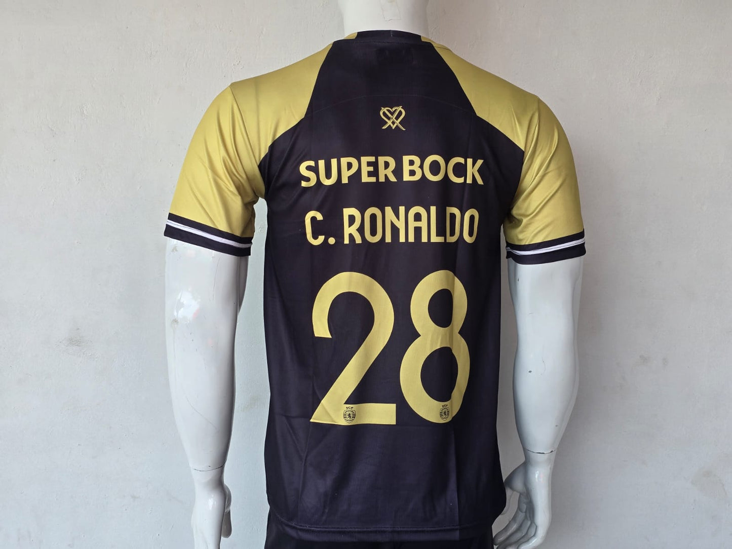 Custom soccer jersey displayed on a mannequin, featuring a dark navy blue body with gold sleeves and gold lettering on the back that reads 'SUPER BOCK', 'C. RONALDO', and '28'.