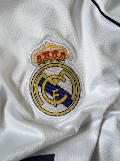 Close-up of a white Real Madrid soccer jersey showing the embroidered club crest with a gold crown on the chest.