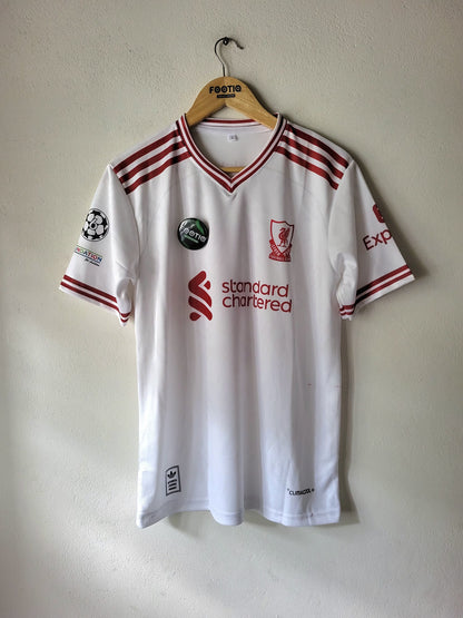 A white Liverpool football jersey with red stripes and logos, hanging on a wooden hanger against a plain wall.