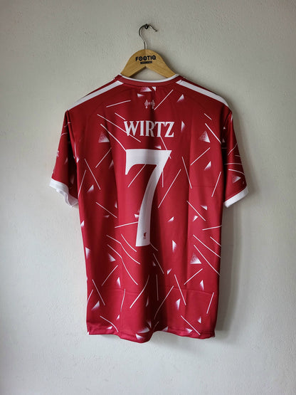 A red soccer jersey with white geometric line patterns, featuring the name 'WIRTZ' and number '7' on the back, hanging on a wooden hanger against a plain wall.