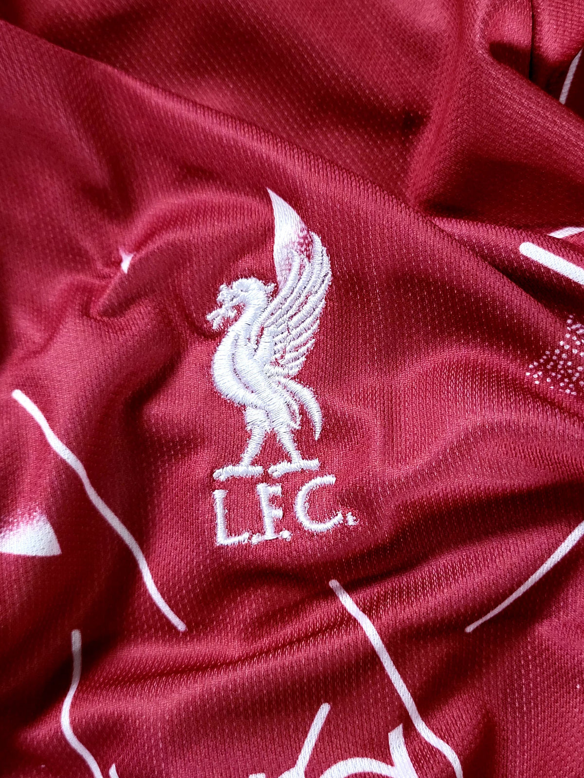 Close-up of a red textured fabric with a white embroidered Liverpool FC bird logo and 'LFC' text.