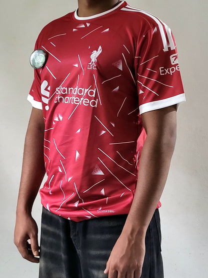 A red and white Liverpool FC short-sleeve soccer jersey worn by a model, featuring the club's crest, 'standard chartered' sponsor logo, and white shoulder stripes.