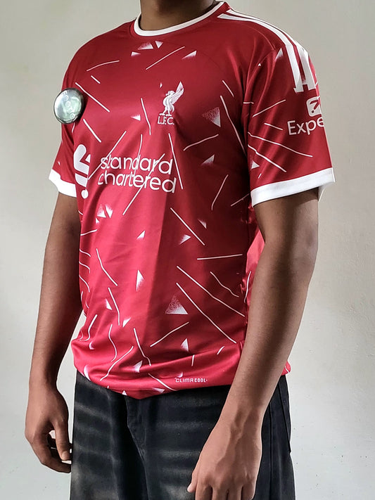 A red and white Liverpool FC short-sleeve soccer jersey worn by a model, featuring the club's crest, 'standard chartered' sponsor logo, and white shoulder stripes.