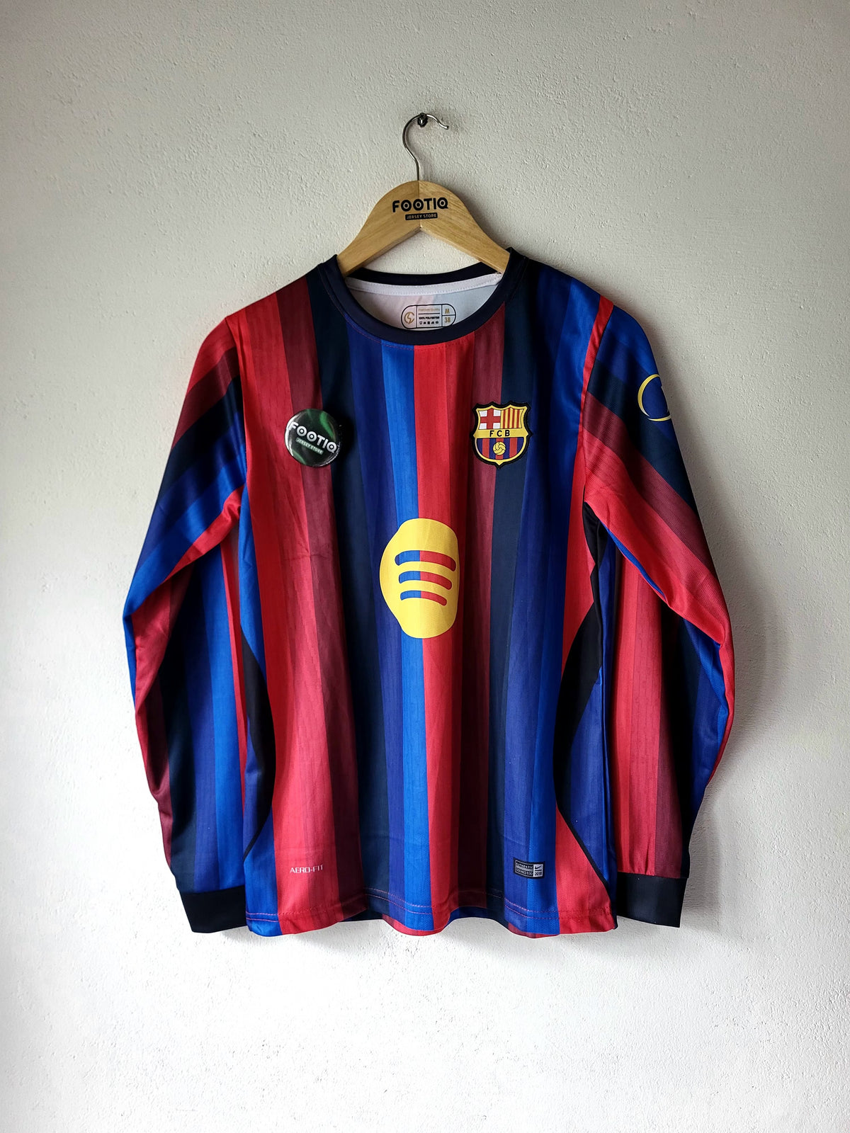 A vintage FC Barcelona long-sleeve soccer jersey with red and blue stripes, hanging on a wooden hanger against a white wall. The jersey features the club's crest on the chest, a yellow sponsor logo, and a circular 'POSTE' badge on the left chest.