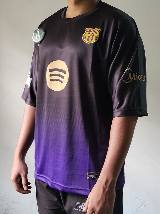 A person wearing a dark purple and black gradient FC Barcelona soccer jersey with gold Spotify and Midea sponsor logos, paired with black shorts.trending jersey, most selling 