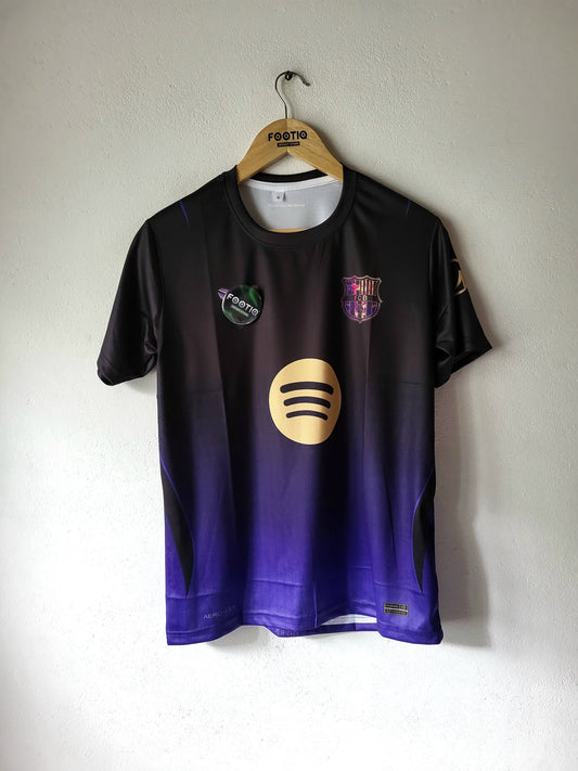 A short-sleeve FC Barcelona soccer jersey hanging on a wooden hanger against a white wall. The jersey features a black-to-purple gradient design with the Spotify logo on the front, the FC Barcelona crest on the chest, and the Feste brand logo on the hanger.
