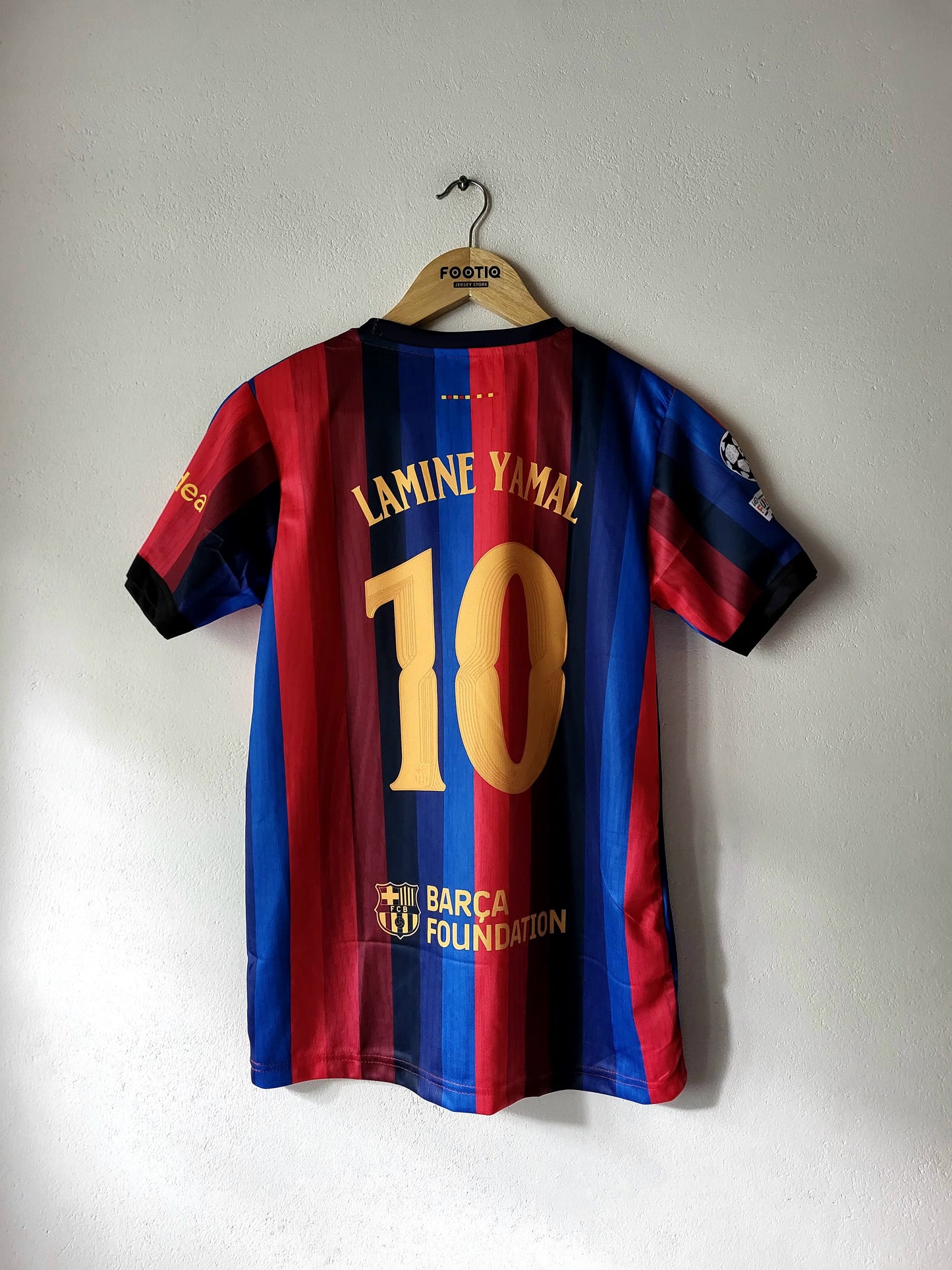 A Barcelona football jersey with the name Lamine Yamal and number 10 printed on the back, hanging on a wooden hanger against a plain wall.