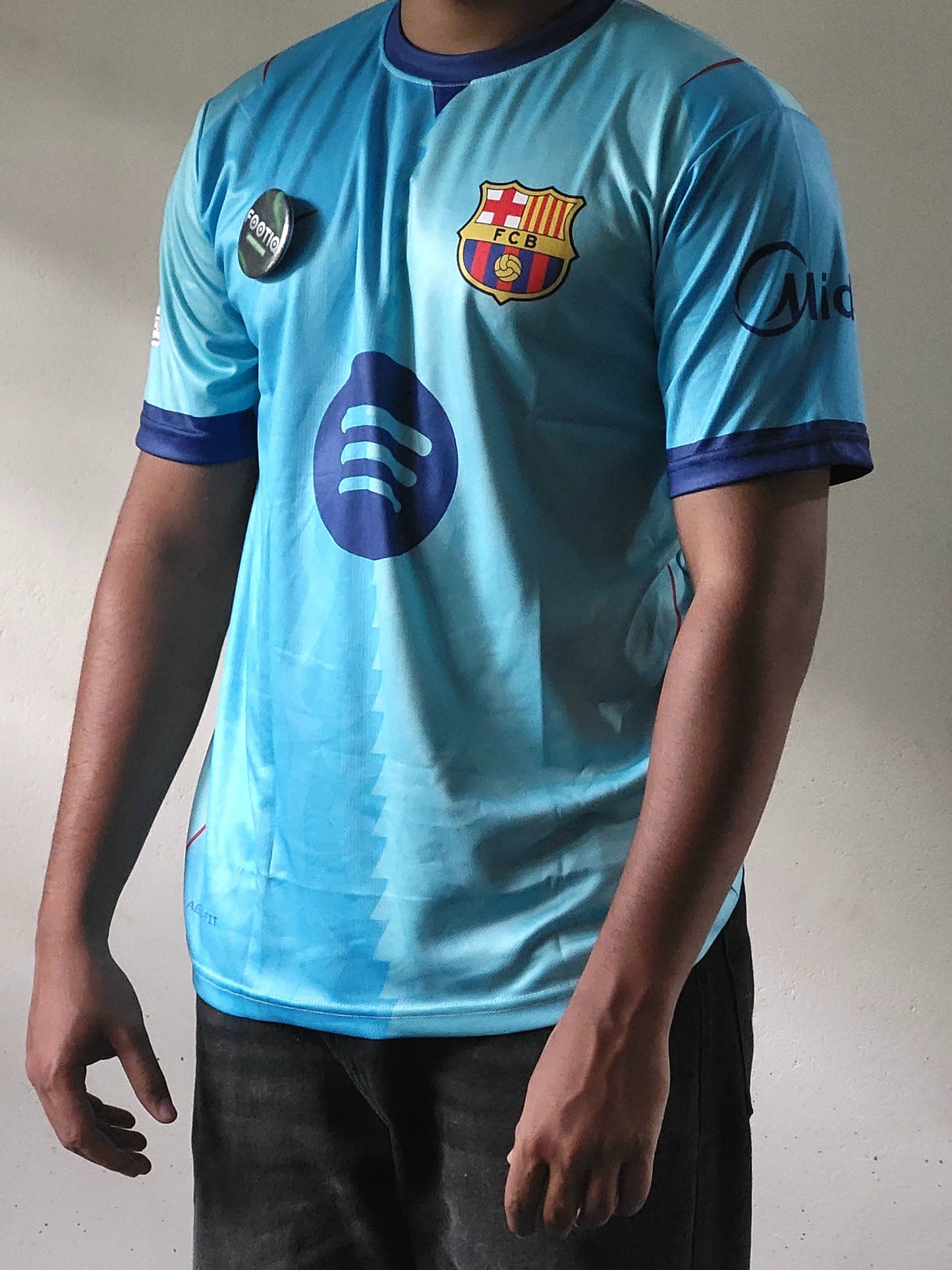 A person wearing a light blue FC Barcelona soccer jersey with dark blue trim, featuring the club crest and Spotify logo on the front.