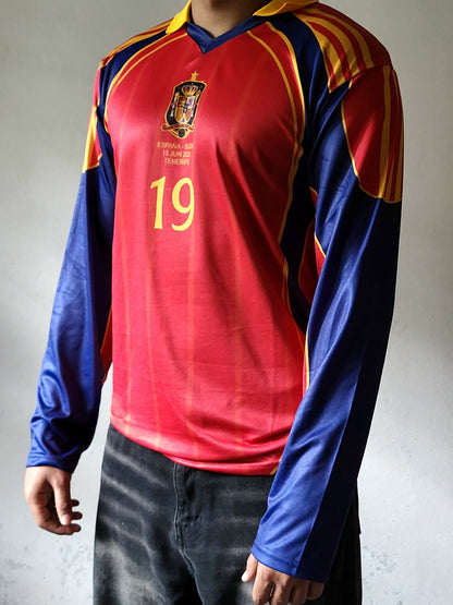 A long-sleeve Spain national football team jersey with a red body, blue sleeves, yellow stripes, and the number 19 printed on the chest, shown on a model.