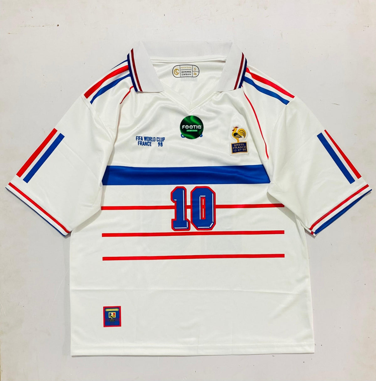 A vintage white France World Cup 1998 soccer jersey with red and blue stripes on the shoulders and sleeves, a blue chest stripe, the number 10 in blue on the front, and various commemorative patches.