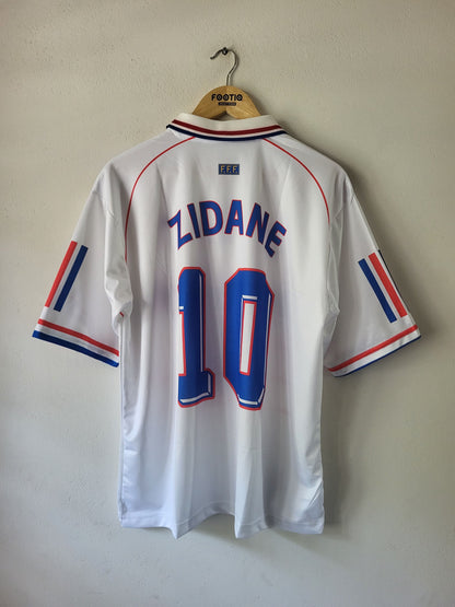 A white France national football team jersey with 'ZIDANE' and the number '10' printed on the back, hanging on a wooden hanger against a plain wall.