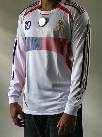A white long-sleeve soccer jersey with red and blue accents, featuring the number 10 on the right chest and a gold rooster crest on the left chest, modeled on a person.