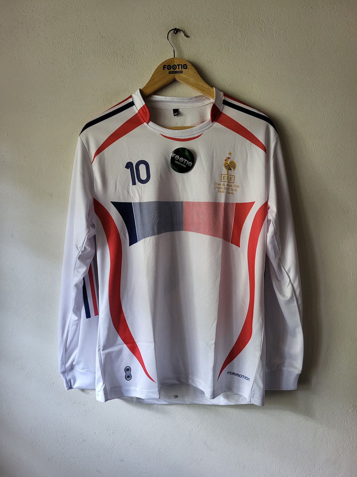A white long-sleeve France soccer jersey with red and navy graphic stripes, featuring the number 10 on the chest, hanging on a wooden hanger against a plain beige wall.